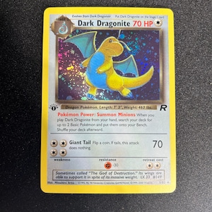 May include: A holographic Dark Dragonite Pokémon card. The card features a yellow and blue dragon-like creature with a 70 HP rating. The card text includes the Pokémon's name, stage, and abilities. The card is a stage 2 evolution.