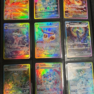 Może przedstawiać: Dziewięć holograficznych kart kolekcjonerskich Pokémon w segregatorze. Karty przedstawiają różne postacie Pokémon, w tym Jolteon, Vaporeon, Flareon, Espeon, Eevee, Umbreon, Leafeon, Sylveon i Glaceon. Każda karta ma unikalny design i schemat kolorów.