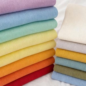 May include: Stacks of folded fabric in various colors, including lavender, blue, green, yellow, orange, and red. A stack of off-white fabric is also visible. The image includes the text "SEARCHANDSHOP Gifts for Everyone".