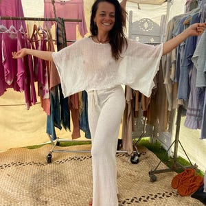 Könnte beinhalten: Ein zweiteiliges Outfit bestehend aus einem weißen, locker sitzenden, halbtransparenten Oberteil mit weiten, kurzen Ärmeln und einer passenden weißen Hose mit hoher Taille, weitem Bein und Kordelzug, gefertigt aus leichtem, strukturiertem Stoff.