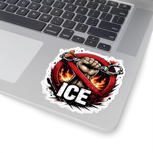 May include: A sticker featuring a graphic design with a red circle and a line through it, with the word "ICE" in white. A fist clenches handcuffs, set against a backdrop of flames. The sticker is on a laptop.