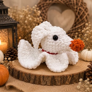 May include: A white crocheted ghost dog plush toy with a round orange nose, black bead eyes, and a thin red collar. The plush features a soft, textured yarn construction with floppy ears and a draped body, capturing a spectral canine appearance.