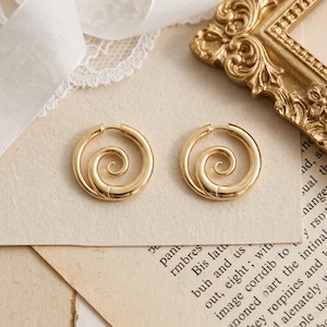 May include: A pair of gold-colored hoop earrings with a spiral design. The earrings are circular with a hinged closure. The spiral design is centered within the hoop. The earrings are displayed on a vintage paper background.