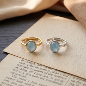 May include: Two adjustable rings featuring oval-shaped, light blue translucent stones. One ring has a polished gold-tone metal band, while the other features a silver-tone metal band. Both rings have an open back design for size adjustment.