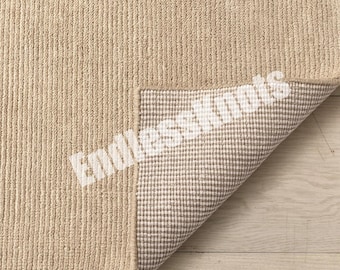 Könnte beinhalten: Ein beigefarbener Teppich mit gerippter, strukturierter Oberfläche. Eine Ecke ist umgeschlagen und zeigt eine weiß-beige karierte Rückseite. Der Text EndlessKnots ist in Weiß über die Mitte der Ecke und die Teppichoberfläche gedruckt.