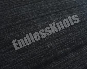 Könnte beinhalten: Ein dunkel anthrazitfarbener Teppich mit einer subtilen horizontalen linearen Textur auf der gesamten Oberfläche. Der Text EndlessKnots ist in einer halbtransparenten weißen Schrift über das Gewebe gelegt.