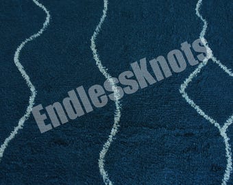Könnte beinhalten: Ein tiefblauer Teppich mit einer strukturierten Hochflor-Oberfläche, der weiße, wellenförmige, vertikale Linien aufweist, die längliche Rautenformen bilden. Der Text EndlessKnots ist in halbtransparenter grauer Schrift über die Mitte gelegt.