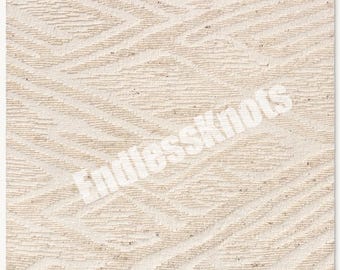Könnte beinhalten: Ein cremefarbenes Textil mit einem erhabenen, strukturierten geometrischen Muster aus diagonalen Linien und Formen. Das Wort EndlessKnots ist in Weiß in der Mitte des Stoffes aufgedruckt, der ein sichtbares Gewebe und kleine dunkle Flecken aufweist.