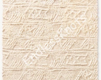 Könnte beinhalten: Ein rechteckiger, cremefarbener Teppich mit einem strukturierten, erhabenen geometrischen Muster aus horizontalen Bändern und diagonalen Linien. Die Oberfläche hat einen zotteligen, getufteten Flor. Der Text "ENDLESS KNOTS" ist diagonal in der Mitte aufgedruckt.