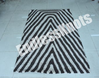 Könnte beinhalten: Ein rechteckiger Teppich mit einem sich wiederholenden Chevron-Muster in Dunkelbraun und Off-White. Das Design besteht aus dicken, strukturierten Streifen in V-Form. Der Text EndlessKnots ist diagonal auf der Oberfläche des Teppichs aufgedruckt.