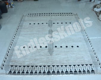 Könnte beinhalten: Ein rechteckiger Teppich mit beigefarbenem Grund und schwarzen geometrischen Mustern. Das Design umfasst eine zentrale vertikale Linie aus Strichen, horizontale Reihen aus schwarzen Rauten und eine Bordüre mit wiederkehrenden Dreiecks- und Linienmotiven.
