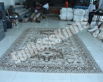 Könnte beinhalten: Ein großer rechteckiger Teppich mit einem zentralen geometrischen Medaillon in Braun- und Cremetönen. Der Teppich zeigt eine detaillierte Bordüre mit sich wiederholenden Mustern und komplexen Motiven auf der gesamten Fläche, flach auf dem Boden.