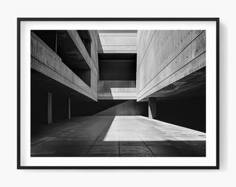 Op de afbeelding: Zwart-wit architectuurfoto van een betonnen gebouw met geometrische vormen en schaduwen. De afbeelding toont een modern, minimalistisch ontwerp met sterke lijnen en een gevoel van diepte. De foto is omlijst in een zwarte rand.