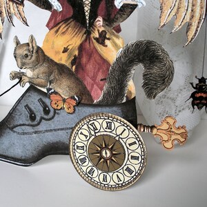 May include: A whimsical mixed media art piece featuring a woman with wings, a squirrel, a clock face, and a beetle. The woman is wearing a long dress with a floral pattern and a crown. The squirrel is sitting on a large black shoe. The clock face is attached to the shoe with a key. The beetle is perched on a white lace fabric.
