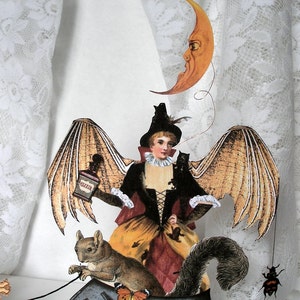 May include: A whimsical Halloween decoration featuring a woman with bat wings, a squirrel, and a crescent moon. The woman is dressed in a brown and red dress with a black bodice and a black hat. She is holding a bottle labeled "Elixir". The squirrel is brown and gray and has a bushy tail. The crescent moon is yellow and has a face.