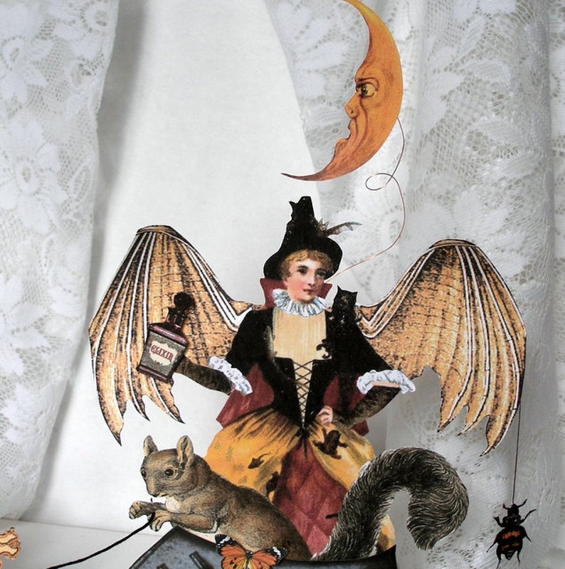 May include: A whimsical Halloween decoration featuring a woman with bat wings, a squirrel, and a crescent moon. The woman is dressed in a brown and red dress with a black bodice and a black hat. She is holding a bottle labeled "Elixir". The squirrel is brown and gray and has a bushy tail. The crescent moon is yellow and has a face.