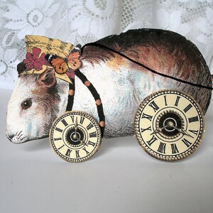 May include: A white and brown toy guinea pig with a straw hat, butterfly, and beaded necklace. The toy has two clock faces on wheels.