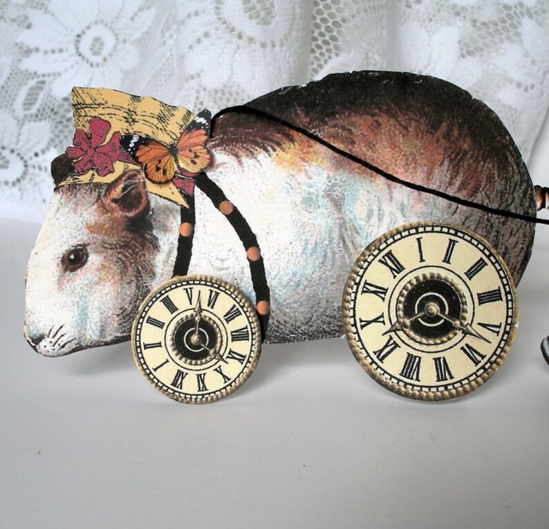 May include: A white and brown toy guinea pig with a straw hat, butterfly, and beaded necklace. The toy has two clock faces on wheels.
