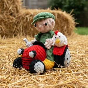 Puede incluir: Muñeco de ganchillo hecho a mano de un granjero con gorra y mono verdes, sentado en un tractor rojo con ruedas negras. Un pollo de ganchillo con cresta roja y cuerpo blanco y negro está junto al granjero. Los juguetes están sobre heno.