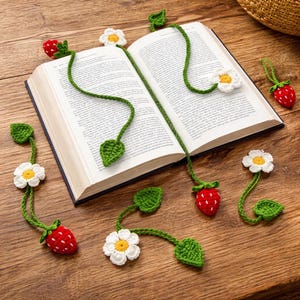 Puede incluir: Marcadores de ganchillo hechos a mano con diseños de fresas, margaritas y hojas en rojo, blanco, amarillo y verde. Los marcadores están colocados alrededor de un libro abierto sobre una superficie de madera, añadiendo un toque encantador a la lectura.