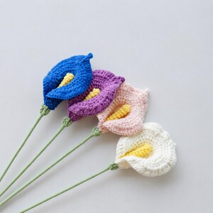 May include: Four handmade crochet calla lilies in blue, purple, pink, and white, each with a yellow center. The stems are green, and the flowers are arranged against a white background. These decorative flowers are perfect for home decor.