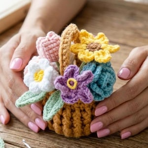 May include: A handmade crochet basket filled with colorful flowers. The basket is brown with a woven texture and a tan handle. The flowers include a pink tulip, white daisy, yellow sunflower, purple flower, and blue flower with green leaves.