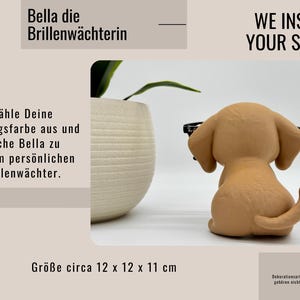 May include: A tan puppy ornament wearing glasses, with the text "WE INSPIRE YOUR STYLE!" and "Bella die Brillenw&auml;chterin." The ornament is approximately 12 x 12 x 11 cm. A decorative item.