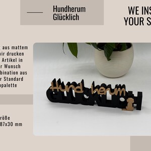 Puede incluir: Un letrero de madera negro y marr&oacute;n que dice "Hundherum Gl&uuml;cklich" con la silueta de un perro. El letrero mide 28 cm x 18,7 cm x 3 cm. Tambi&eacute;n se ve el texto "WE INSPIRE YOUR STYLE!".