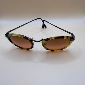 May include: Oval-shaped sunglasses with a tortoiseshell pattern on the frames and brown-tinted lenses. The frames are accented with black metal arms and a bridge. A stylish accessory for eye protection.