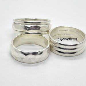 May include: Three silver rings with a polished finish. One ring features a hammered texture, while the other two display smooth, stacked bands. The text Skjewellerss is visible on the surface of one of the smooth rings. These rings are metallic.