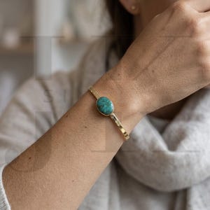 Peut inclure: Bracelet doré orné d'une pierre ovale turquoise. Le bracelet présente une texture martelée et un design simple et élégant. La pierre turquoise est d'un bleu-vert vibrant.