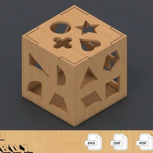 May include: A wooden shape sorter cube with various cut-out shapes on each side, including a circle, star, heart, and cross. The cube is made of light-colored wood and sits on a dark gray surface. The text "ATACAN WOOD-BOX" is at the bottom.