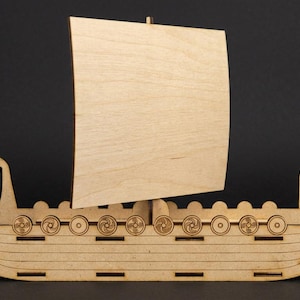 May include: A wooden Viking ship model with a light-colored sail and intricate cut-out details. The ship features a detailed hull, decorative carvings, and a stylized dragon head at the bow. The model is set against a dark background.