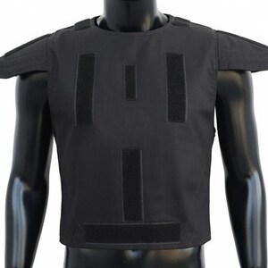 Peut inclure: Gilet tactique noir avec épaulettes et plusieurs panneaux Velcro. Le gilet est présenté sur un mannequin. Le gilet est conçu pour la protection et a un design épuré et fonctionnel.