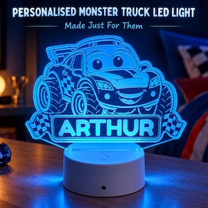 May include: A blue LED light featuring an etched monster truck design with the name ARTHUR displayed on a banner. The acrylic light sits on a round white base with a power button, emitting a bright blue glow in a dark room setting.