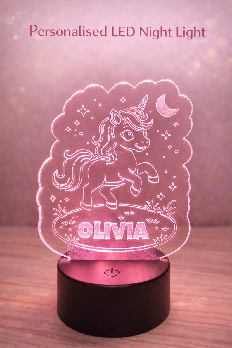 May include: Personalised LED night light with a unicorn design. The light is pink and features the name "OLIVIA" in a decorative font. The unicorn is outlined in white and has a horn, mane, and tail. The base is black.