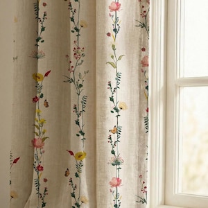 Peut inclure: Un rideau beige orné de rangées verticales de fleurs sauvages brodées dans des tons de rose, jaune et rouge, entremêlées de petits papillons orange et de tiges vertes, suspendu près d'un cadre de fenêtre blanc avec une texture de tissu visible.