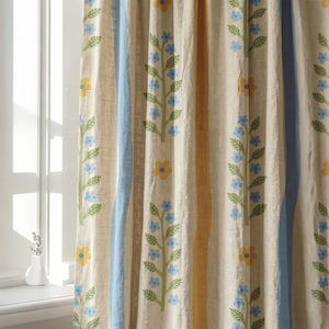 May include: A beige curtain panel featuring vertical stripes of light blue and mustard yellow, interspersed with repeating patterns of vertical green stems adorned with small light blue flowers and larger yellow blossoms in a simple design.