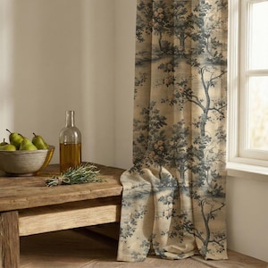 May include: A floor-length curtain featuring a dark blue and beige toile pattern of trees and flowers. Beside the curtain sits a clear glass bottle filled with golden liquid and a gray bowl containing several green pears and a sprig of rosemary.