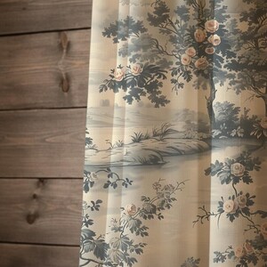 May include: A sheer curtain panel featuring a toile-inspired print with muted blue-grey landscape scenes, including trees and rolling hills, accented by soft pink floral blossoms scattered across a light cream-colored fabric background.