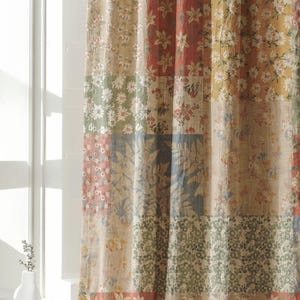 Puede incluir: Una cortina con un diseño de patchwork compuesto por varios paneles de tela rectangulares. Cada panel muestra un patrón floral distinto en tonos apagados de rojo, amarillo, azul, verde y beige, creando una superficie textil multicolor.