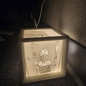 May include: A lit wooden box with a picture of a child holding a sign that says "First Day of Kindergarten". The box is illuminated from within, creating a warm glow. The image is a portrait of a child in a school setting.