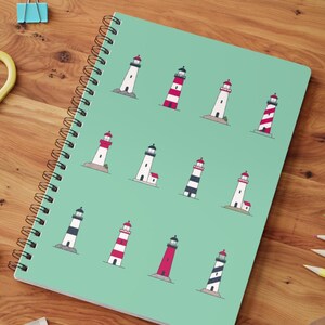 Op de afbeelding: Een spiraalgebonden notitieboek met een turquoise omslag met een patroon van verschillende vuurtorenillustraties. De vuurtorens zijn afgebeeld in rood, wit, zwart en grijs, sommige met gestreepte ontwerpen. Het notitieboek ligt open op een houten oppervlak.