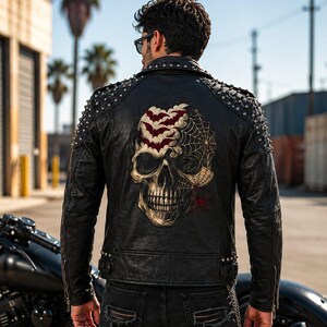 May include: A black leather jacket featuring silver metal studs on the shoulders and collar. The back displays a large graphic print of a human skull partially covered by a spider web and a cluster of red bats, paired with distressed black denim jeans.