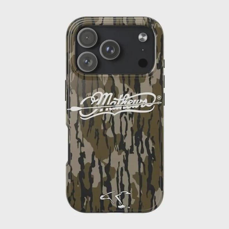 K&ouml;nnte beinhalten: Eine Handyh&uuml;lle mit Camouflage-Muster, mit dem wei&szlig;en Schriftzug "Mathews", einem Pfeil und einem Entenlogo. Die H&uuml;lle hat eine gl&auml;nzende Oberfl&auml;che und einen Kameraausschnitt.