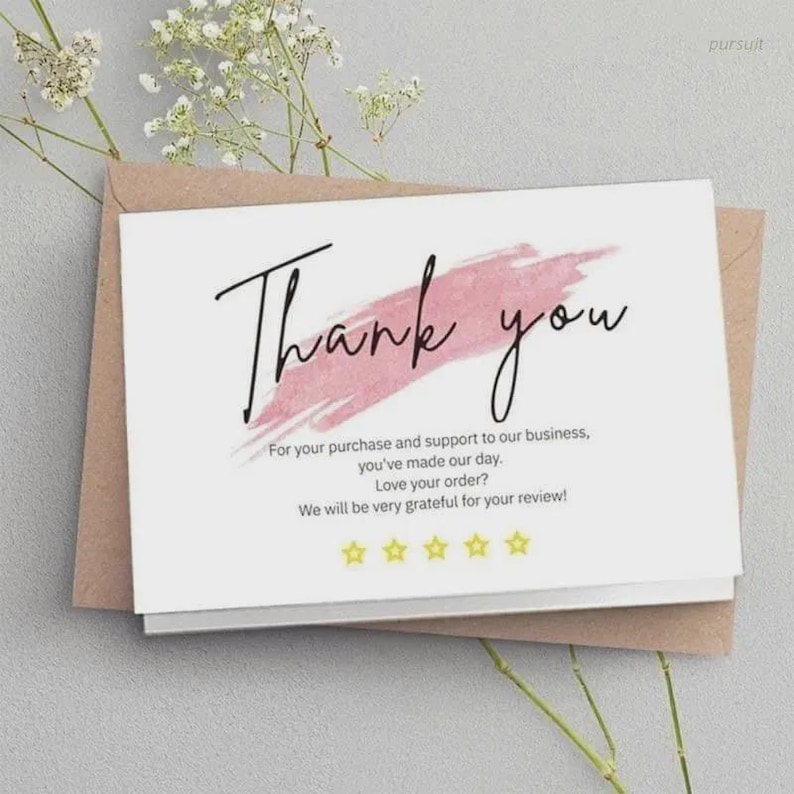 K&ouml;nnte beinhalten: Eine wei&szlig;e Karte mit den Worten "Thank you" in schwarzer Schrift, akzentuiert durch einen rosa Pinselstrich. Die Karte befindet sich in einem braunen Umschlag, mit Text darunter, der dem Kunden dankt und um eine Bewertung bittet. Florale Akzente sind sichtbar.