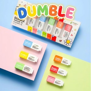Könnte beinhalten: Ein Set mit Dumble Inhaler V2 Produkten. Auf der Box steht das Wort "DUMBLE" in bunten Buchstaben. Einzelne Inhalatoren sind in Blau, Gelb, Grün, Orange, Rot und Rosa gehalten. Produktname und Details sind auf jedem Inhalator aufgedruckt.
