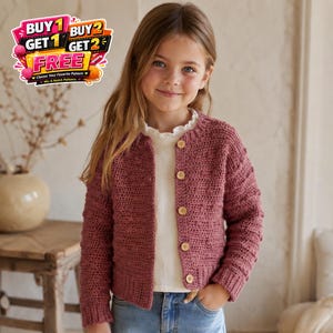 May include: A young girl wearing a dusty rose-colored, button-down crochet cardigan. The cardigan has a textured stitch pattern and wooden buttons. She is wearing a white top and blue jeans. The image includes text that says "BUY 1 GET 1 FREE" and "BUY 2 GET 2 FREE".