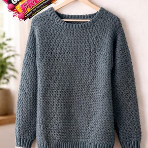 Puede incluir: Un suéter de punto gris azulado con un patrón de puntada texturizada, exhibido en una percha de madera. El suéter tiene cuello redondo y puños y dobladillo acanalados. La imagen incluye un gráfico promocional con el texto "BUY 1 GET 1 FREE".