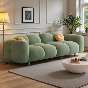 Puede incluir: Un sofá moderno verde claro con un diseño único y redondeado. El sofá tiene múltiples secciones y se acentúa con dos cojines naranjas. Se apoya sobre patas plateadas en un salón bien iluminado. La longitud del sofá es de aproximadamente 250 cm.